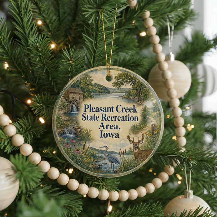 A circular ornament hanging on a Christmas tree, featuring a scenic landscape with a bird, a deer, and a waterfall.