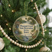 A circular ornament hanging on a Christmas tree, featuring a scenic landscape with a bird, a deer, and a waterfall.