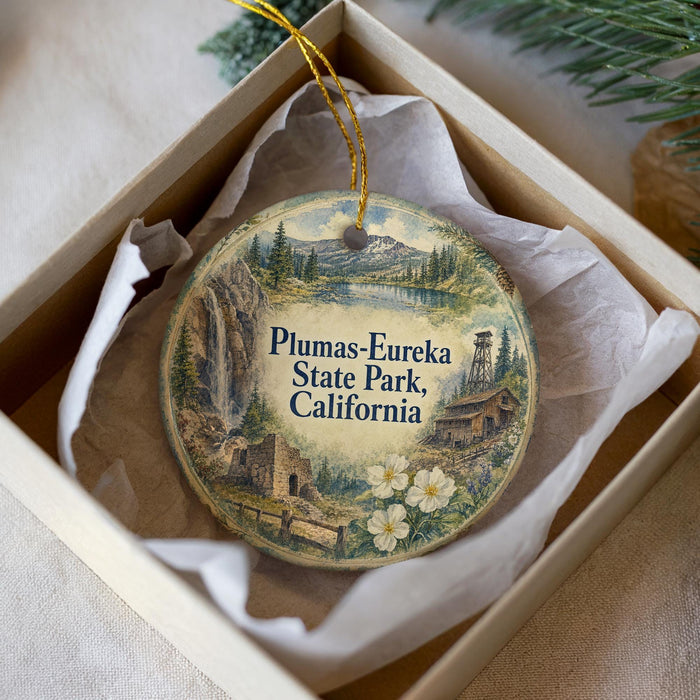 A decorative ornament in a box, featuring a scenic landscape with mountains, a waterfall, and a small building.