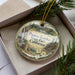 A decorative ornament in a box, featuring a scenic landscape with buildings and trees, and the text "Plumas-Eureka State Park, California" printed on it.