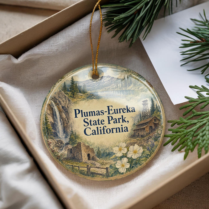A decorative ornament with a scenic landscape of Plumas-Eureka State Park, California, featuring a waterfall, pine trees, and a cabin.
