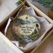 A decorative ornament in a box, featuring a scenic landscape with a mountain range, a river, and a bird of prey.