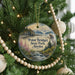 A round ornament hanging on a Christmas tree, featuring a scenic landscape with mountains, a river, and a bird in flight.