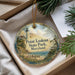 A decorative ornament with a lighthouse and a scenic landscape, placed in a box with pine branches.