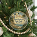 A round ornament hanging on a Christmas tree, featuring a lighthouse and a coastal landscape.