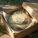 A round ornament in a box, featuring a tropical beach scene with palm trees and mountains, and the text "Polihale State Park, Hawaii".