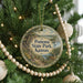 A round ornament hanging on a Christmas tree, featuring a scenic landscape with a path, a body of water, and a boat.