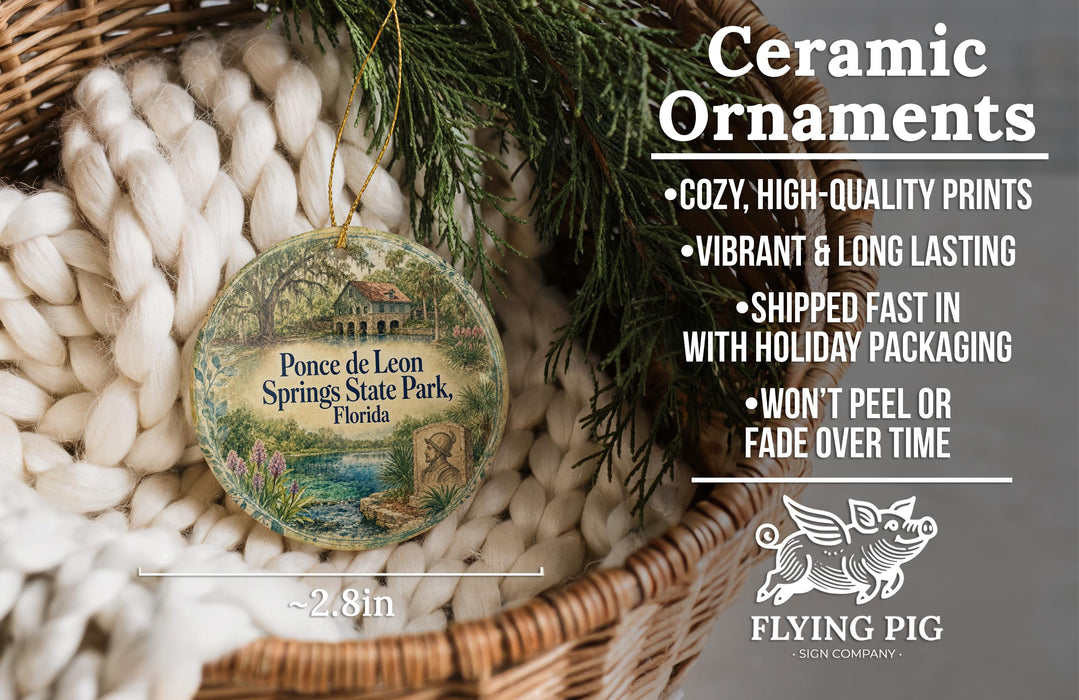 Ceramic ornaments, featuring a round ornament with a house and trees, are displayed in a basket with a woven blanket.