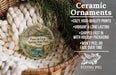 Ceramic ornaments, featuring a round ornament with a house and trees, are displayed in a basket with a woven blanket.