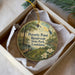 A round ornament with a painting of a park scene, including a pond, trees, and a bird, is displayed in a box.