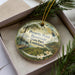 A decorative ornament with a landscape scene featuring a pond, trees, and flowers, along with text that reads "Poverty Point Reservoir State Park Louisiana".