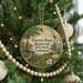 A round ornament hanging on a Christmas tree, featuring a scenic landscape with a river, trees, and birds.