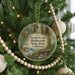 A round ornament hanging on a Christmas tree, featuring an illustration of a forest scene with an owl.