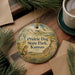 A decorative ornament featuring a prairie dog and the text "Prairie Dog State Park, Kansas" is displayed on a wooden surface, accompanied by pine branches and a cup of coffee.