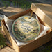 A decorative ornament in a wooden box, featuring a scenic landscape with a house and flowers, with the text "Prairie Rose State Park, Iowa" printed on it.