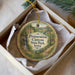 A decorative ornament in a box, featuring a scenic landscape with a waterfall and a path leading through the woods.