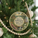 A round ornament hanging on a Christmas tree, featuring a scenic landscape with a waterfall and a house.