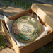 A decorative ornament in a box, featuring a scenic image of Radium Springs State Park in Georgia.