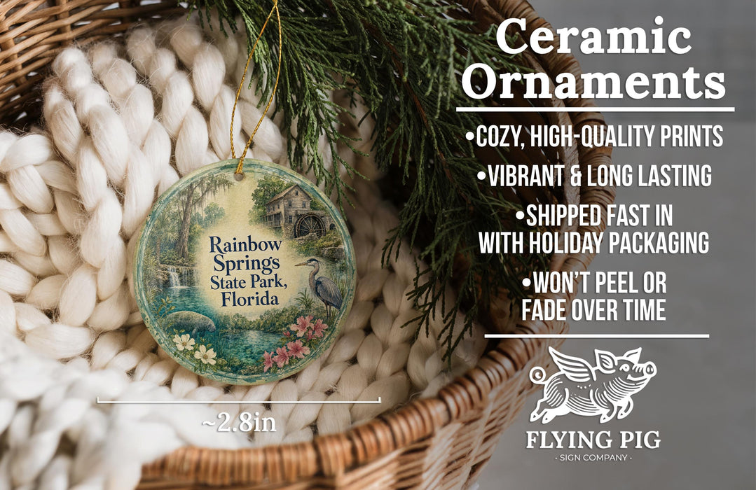 Ceramic ornaments, featuring a round ornament with a painting of a house and a bird, hanging in a basket with pine branches.