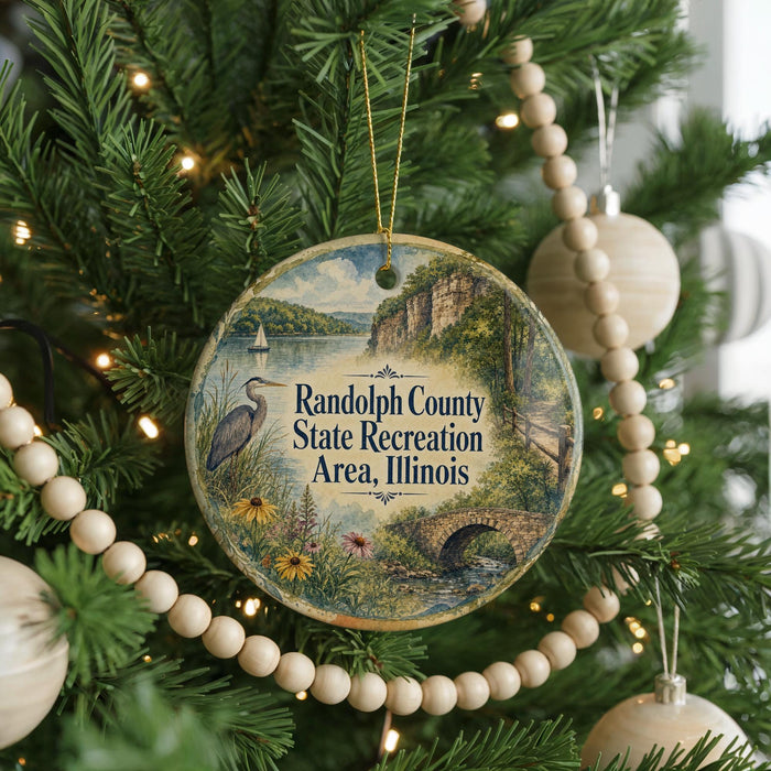 A round ornament hanging on a Christmas tree, featuring a scenic landscape with a lake, mountains, and a bird.