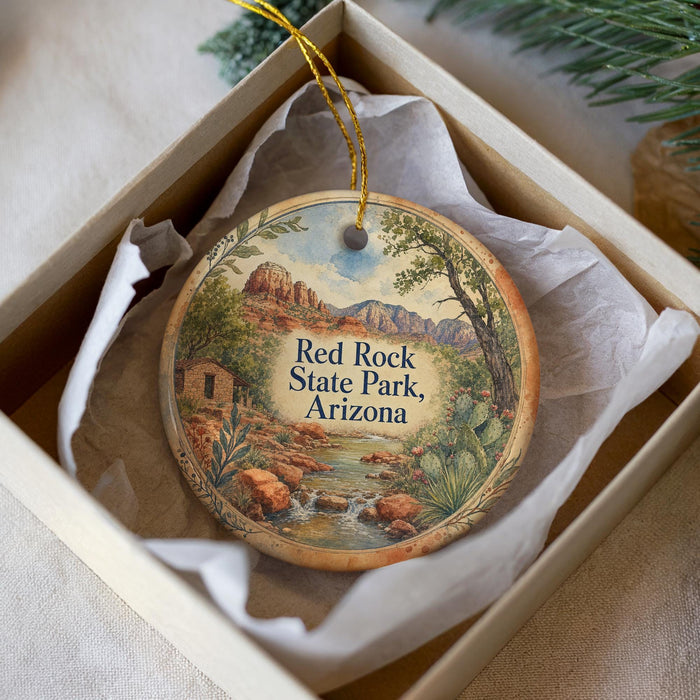 A decorative ornament in a white box, featuring a scenic landscape with mountains, trees, and a stream.