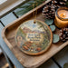 A decorative ornament featuring a scenic landscape of Red Rock State Park, Arizona, with pine cones and a lit candle on a wooden tray.