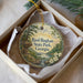 A decorative ornament in a box, featuring a scenic landscape with a river, trees, and mountains.