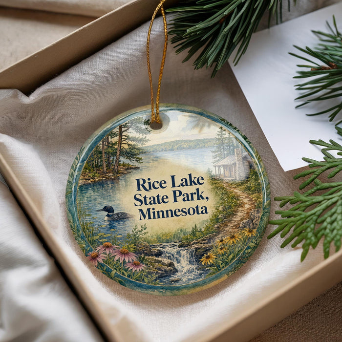 A decorative ornament with a scenic landscape of Rice Lake State Park, Minnesota, featuring a lake, a path, and a bird.