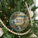 A round ornament hanging on a Christmas tree, featuring a scenic landscape with a lake, trees, and a waterfall.