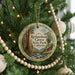 A round ornament hanging on a Christmas tree, featuring a scenic image of a forest with a large tree and a stream.