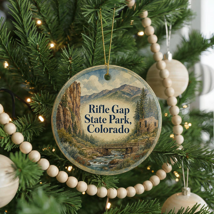 A round ornament hanging on a Christmas tree, featuring a scenic landscape with mountains and a river.