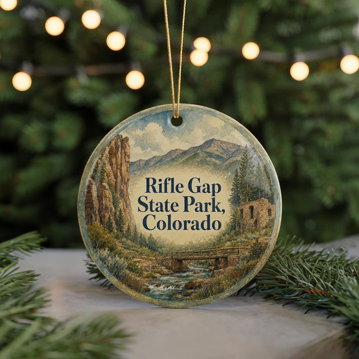 A round ornament with a painting of a mountain landscape and the text "Rifle Gap State Park, Colorado" on it, hanging from a string.