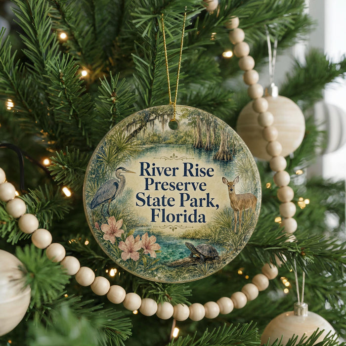 A round ornament hanging on a Christmas tree, featuring illustrations of a bird, a deer, and flowers, with the text "River Rise Preserve State Park, Florida" displayed on it.