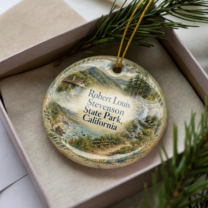A decorative ornament in a box, featuring a scenic landscape with mountains, trees, and a river.