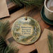 A decorative ornament featuring a scenic landscape with a house, trees, and a waterfall, hanging on a wooden surface.