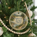 A round ornament on a Christmas tree, featuring a scenic landscape with mountains, a river, and a cabin.