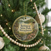 A round ornament hanging on a Christmas tree, featuring a scenic landscape with a castle, trees, and a river.
