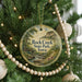 A round ornament hanging on a Christmas tree, featuring a scenic landscape with a river, bridge, and mountains.