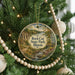 A round ornament hanging on a Christmas tree, featuring a scenic landscape with a river and mountains.