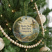 A round ornament hanging on a Christmas tree, featuring a scenic landscape with a lighthouse and a body of water.