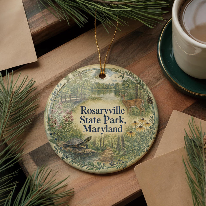 A decorative ornament with a nature scene, featuring a turtle, a deer, and a bird, hangs on a wooden surface alongside a cup of coffee and some pine branches.