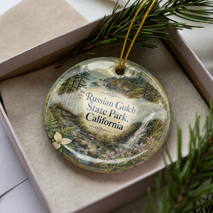 A decorative ornament with a landscape scene featuring a waterfall and pine trees, placed in a box with a pine branch.