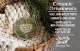 Ceramic ornaments, including a round ornament with a tropical scene and text, are displayed in a basket with greenery.