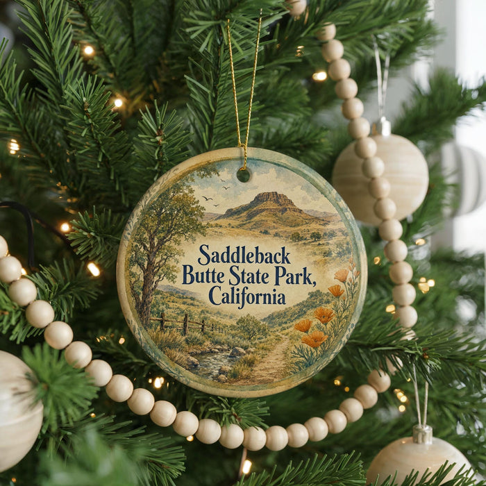 A round ornament hanging on a Christmas tree, featuring a scenic landscape with a mountain and a stream.