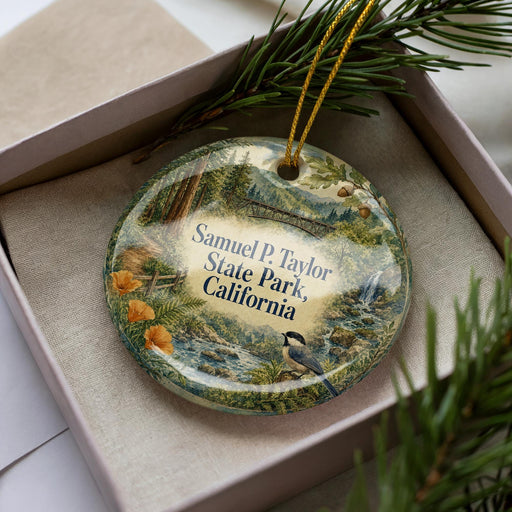A decorative ornament in a box, featuring a scenic landscape with pine trees, a bird, and a river.