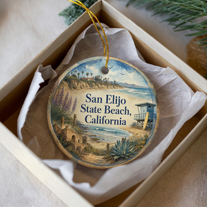 A decorative ornament in a box, featuring a beach scene with palm trees, a lifeguard tower, and a sandy beach.