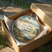 A decorative ornament in a box, featuring a beach scene with palm trees and a lifeguard tower, along with the text "San Elijo State Beach, California".