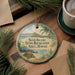 A round ornament with a beach scene and palm trees, featuring the text "Sand Island State Recreation Area, Hawaii" on it, is displayed on a wooden surface alongside a cup of coffee and some pine branches.