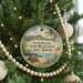 A round ornament hanging on a Christmas tree, featuring a beach scene with palm trees and a mountain in the background.