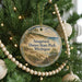 A round ornament hanging on a Christmas tree, featuring a scenic image of a beach and dunes.